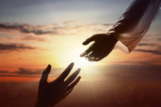 Jesus Christ giving a helping hand to human with a sunset sky background